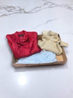 Ropa vintage en caja sorpresa con prendas de cuero y tejidos en tonos rojos, beige y azul.